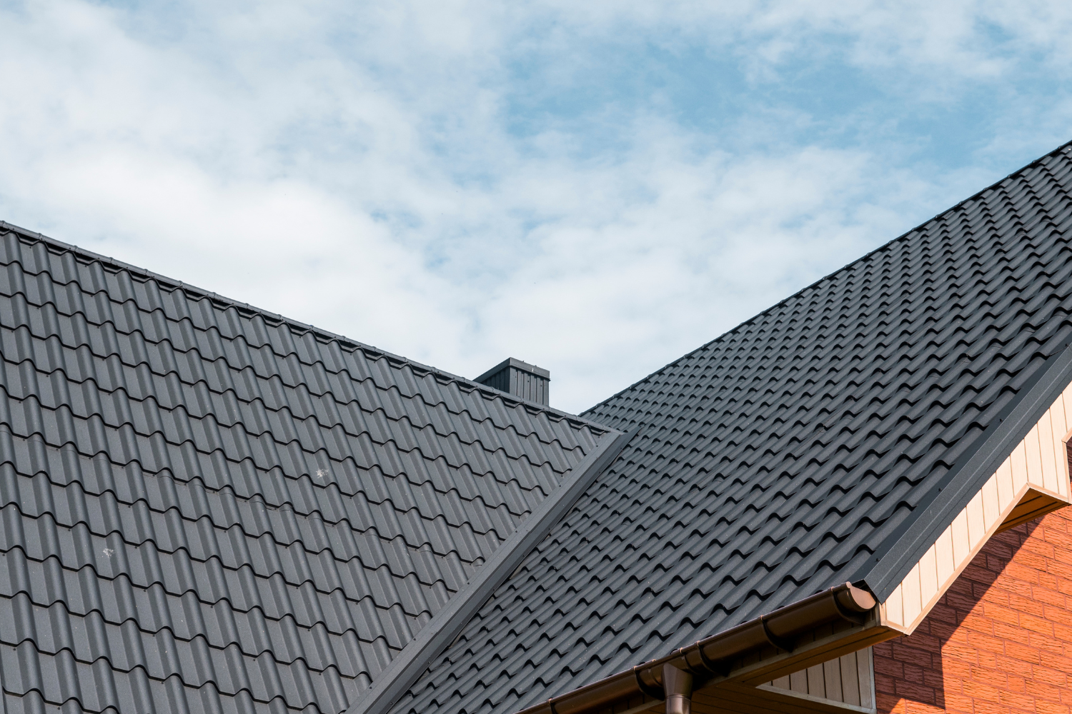 Dark gray tiled rooftops against a cloudy blue sky, with a brick wall at right