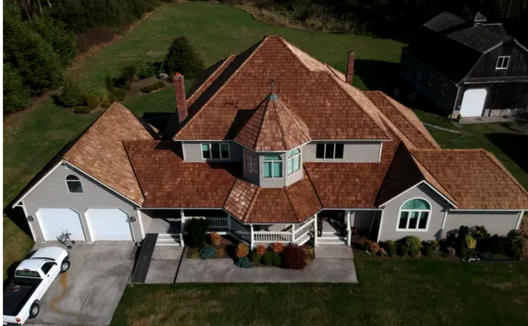 Aerial view of a large house with a red shingle roof, white garage, and landscaped front yard.