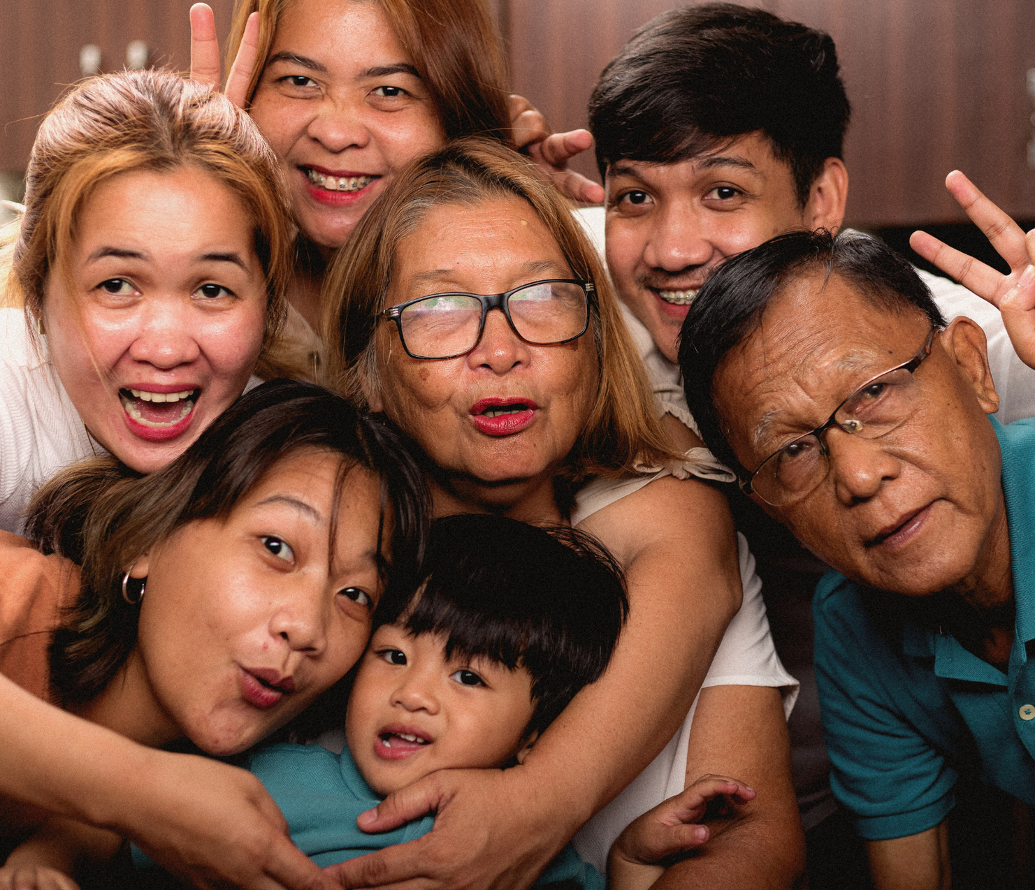 Six people pose closely together, smiling and making playful faces indoors.
