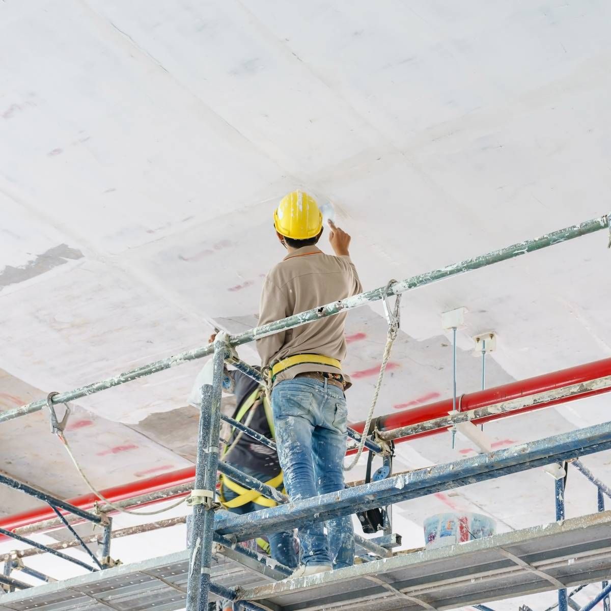 A construction worker is standing on a scaffolding painting the ceiling.