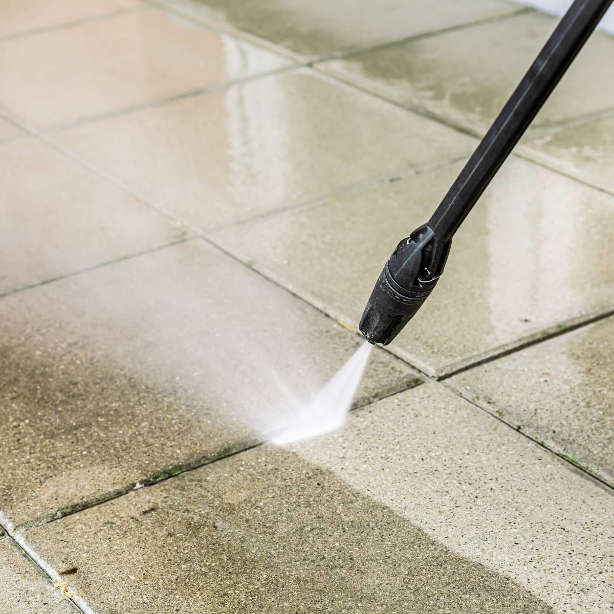 A person is using a high pressure washer to clean a tiled floor.