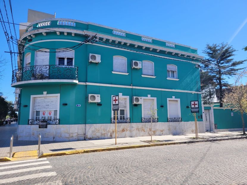 Edificio de esquina de dos plantas de color turquesa con molduras y ventanas blancas bajo un cielo azul claro.