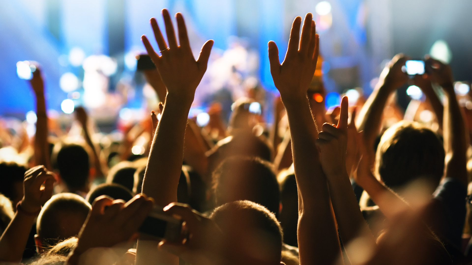 Crowd at a concert with raised hands and blurred stage lights in the background