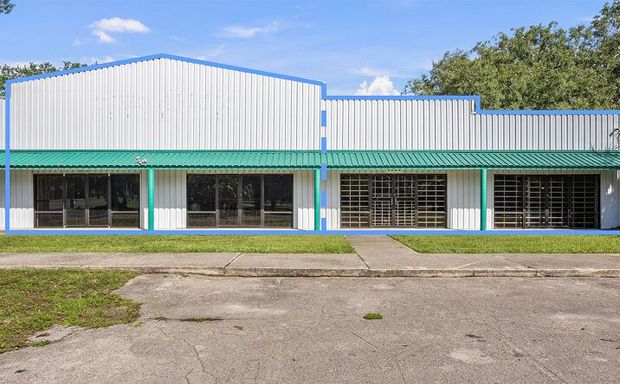 Empty storefront with white corrugated facade, turquoise trim, and large windows along a cracked parking lot