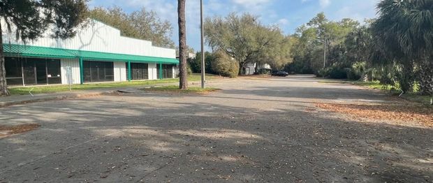Empty gravel lot beside a low green-and-white building with trees in the background