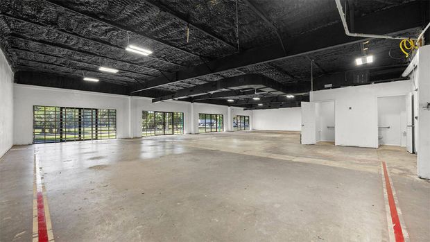 Empty indoor warehouse space with concrete floor, black ceiling, white walls, and large windows.