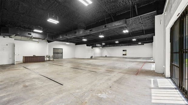 Empty industrial warehouse with concrete floor, white walls, and black ceiling lights