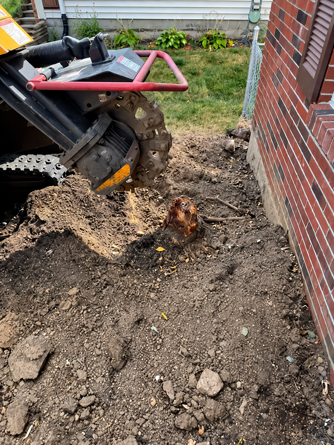 Bulldozer clearing dirt beside a brick house, with a small tree stump in the yard. Bulldozer clearing dirt beside a brick house, with a small tree stump in the yard.