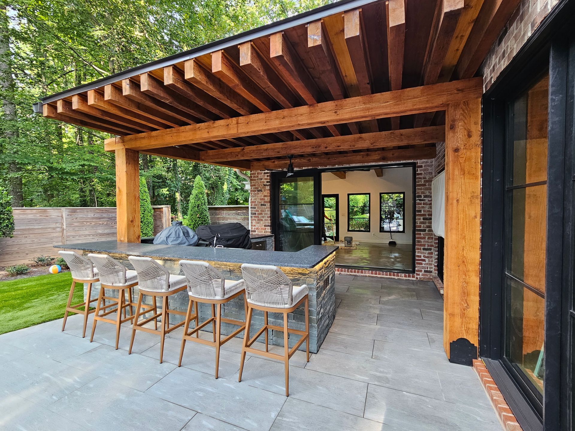 A patio with a bar and stools under a wooden roof.