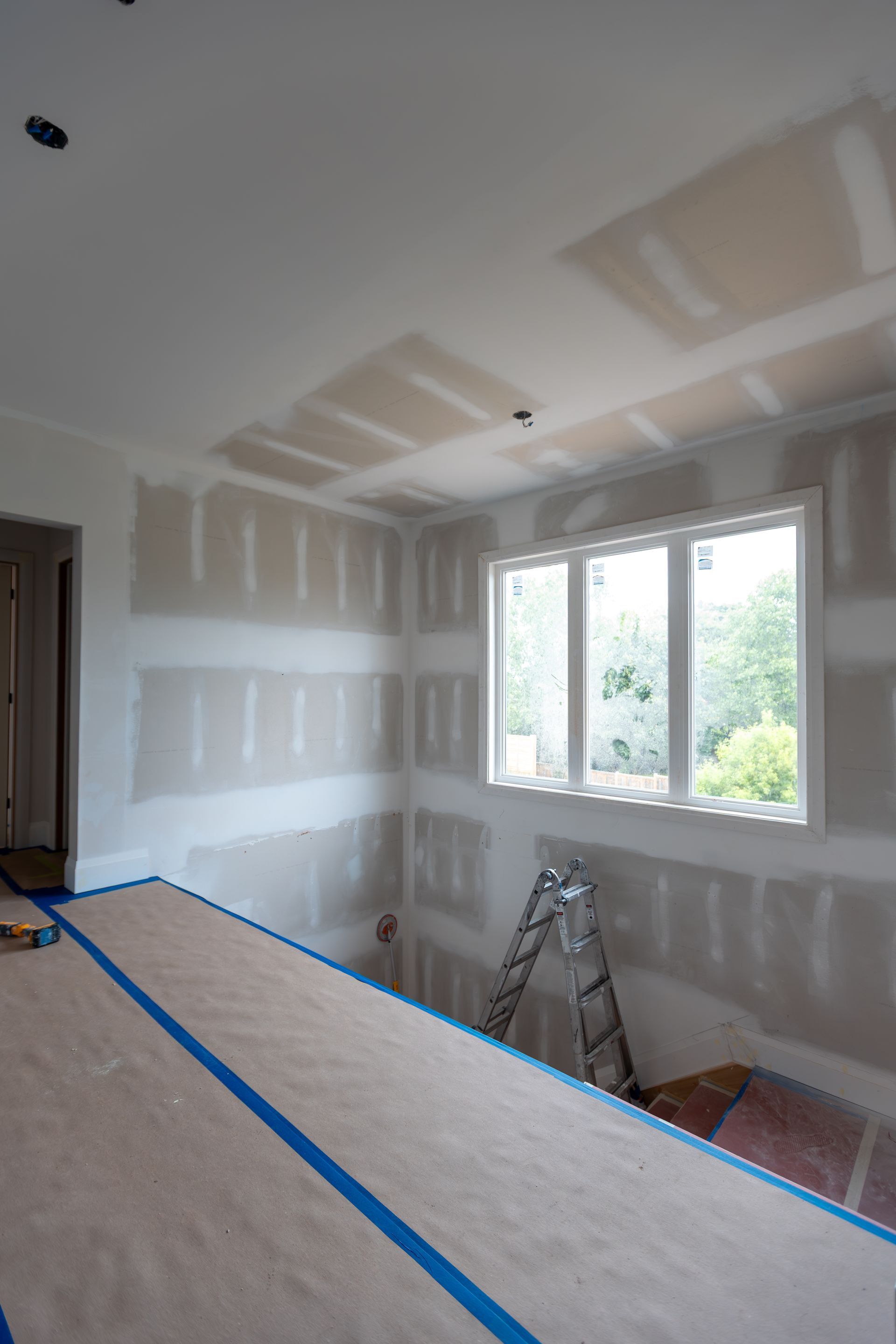 Interior construction with drywall on walls and ceiling, window, ladder, and taped surface.