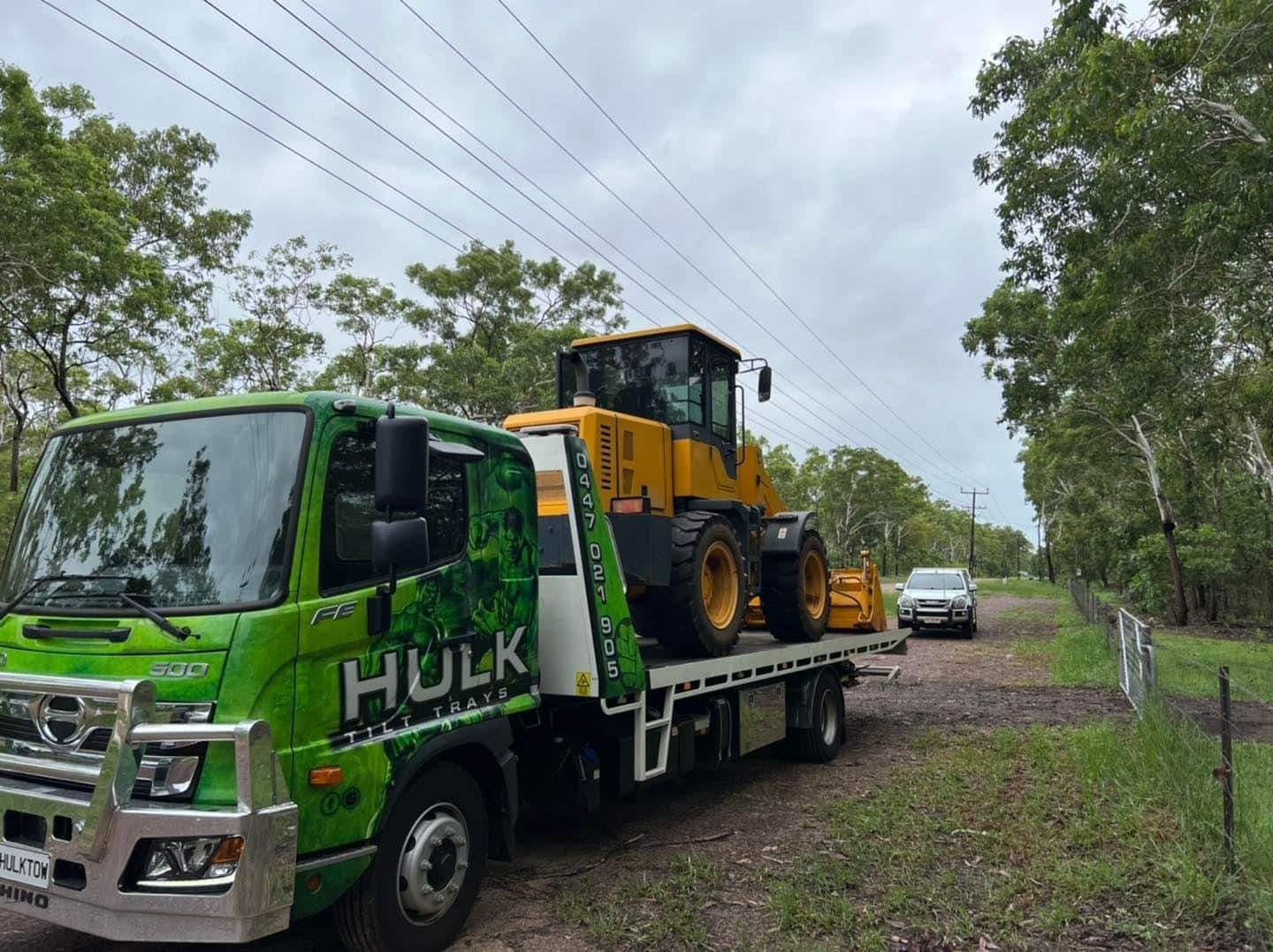 A Green Tow Truck with A Yellow Tractor on The Back Is Parked on A Dirt Road — Hulk Tilt Trays In Humpty Doo, NT