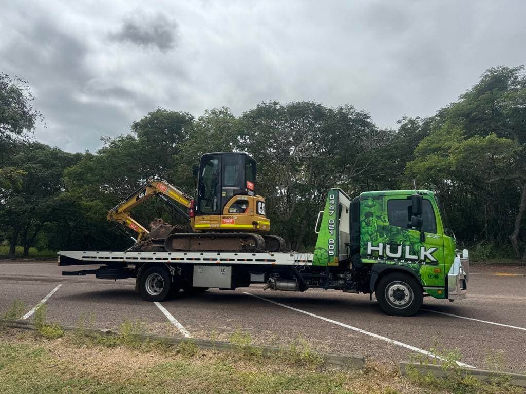A Tow Truck with A Small Excavator on The Back Is Parked in A Parking Lot — Hulk Tilt Trays In Humpty Doo, NT