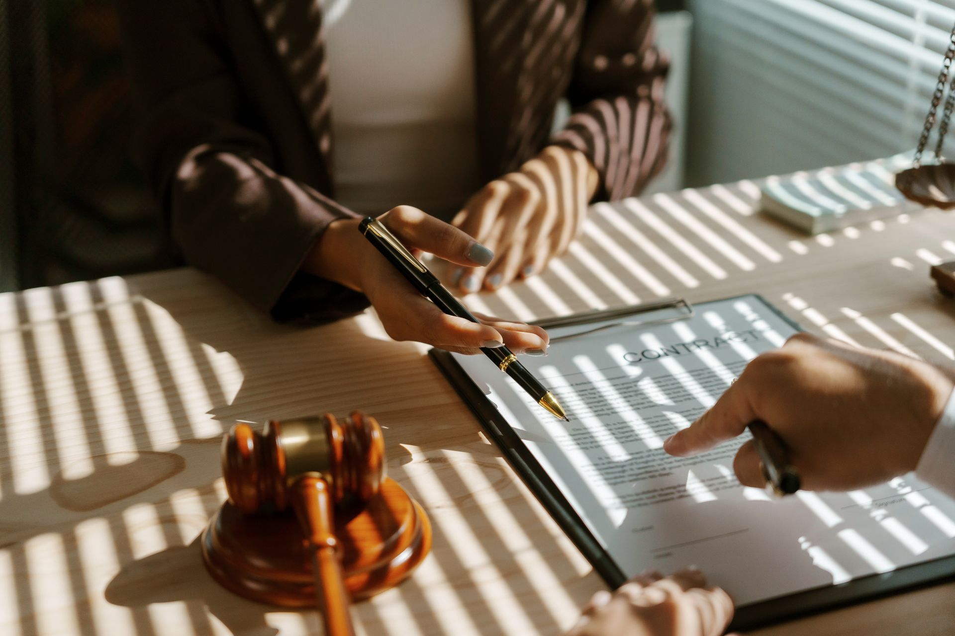 Two hands over a document at a desk with a gavel, striped sunlight across the table Two hands over a document at a desk with a gavel, striped sunlight across the table