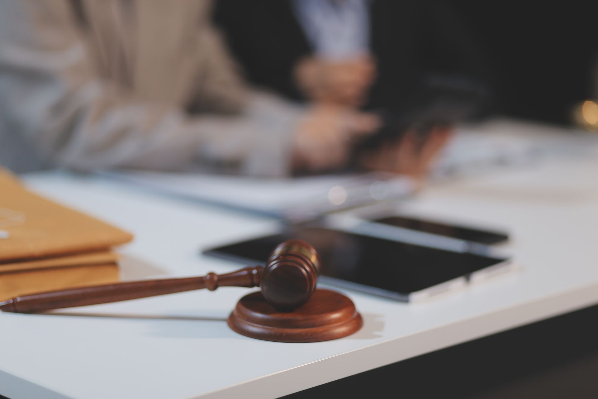 Judge’s gavel on a white desk with a smartphone and blurred people in the background Judge’s gavel on a white desk with a smartphone and blurred people in the background