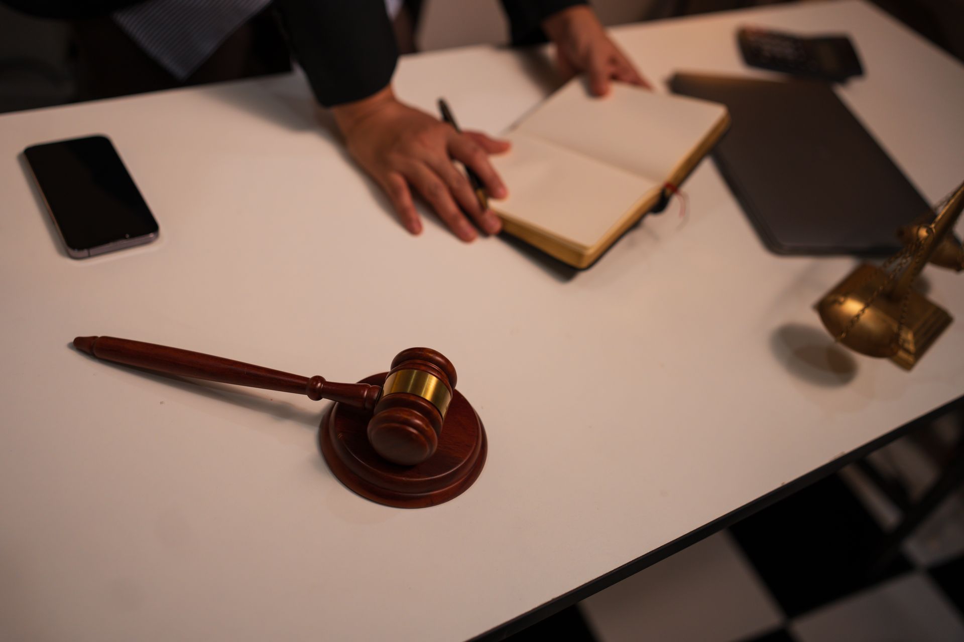 Judge’s gavel on a desk beside a notebook and smartphone, with a hand reaching toward the notebook. Judge’s gavel on a desk beside a notebook and smartphone, with a hand reaching toward the notebook.