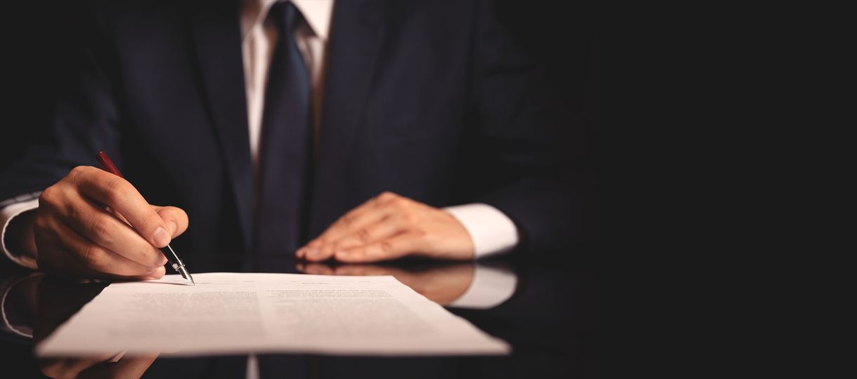 Business person signing a document at a desk with a pen Business person signing a document at a desk with a pen