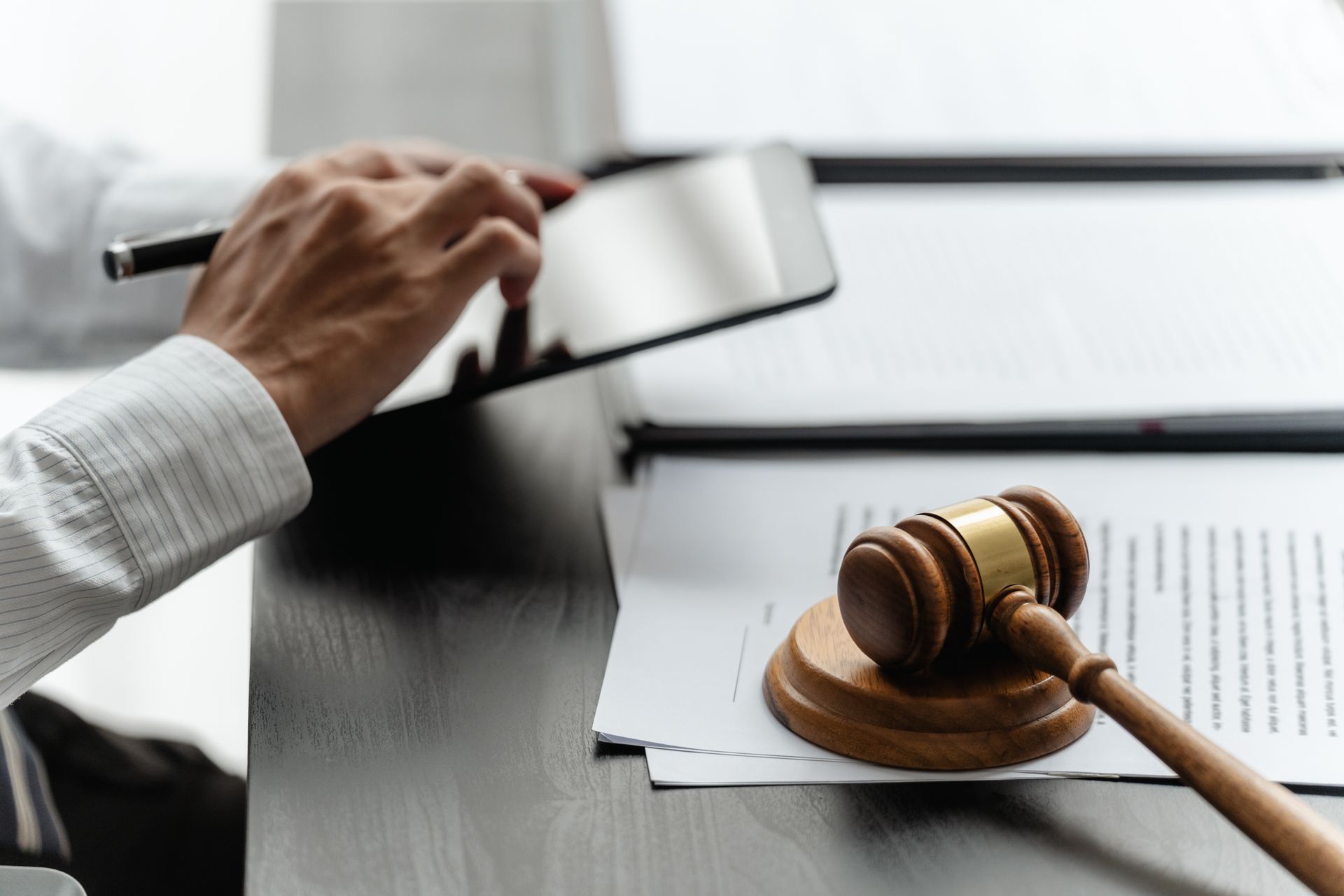 Hand holding a gavel over documents beside a judge’s gavel on a desk Hand holding a gavel over documents beside a judge’s gavel on a desk