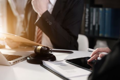 Lawyer’s desk with gavel, laptop, and notebook as two people review documents Lawyer’s desk with gavel, laptop, and notebook as two people review documents