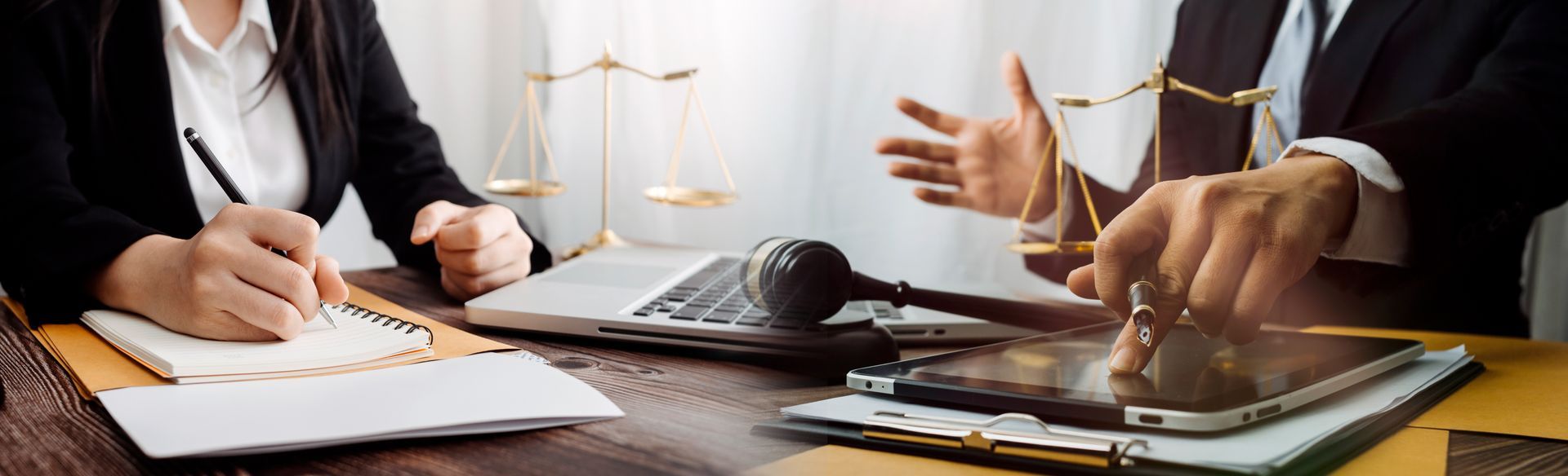 Two people reviewing documents at a desk with a laptop and scales of justice in a legal office Two people reviewing documents at a desk with a laptop and scales of justice in a legal office