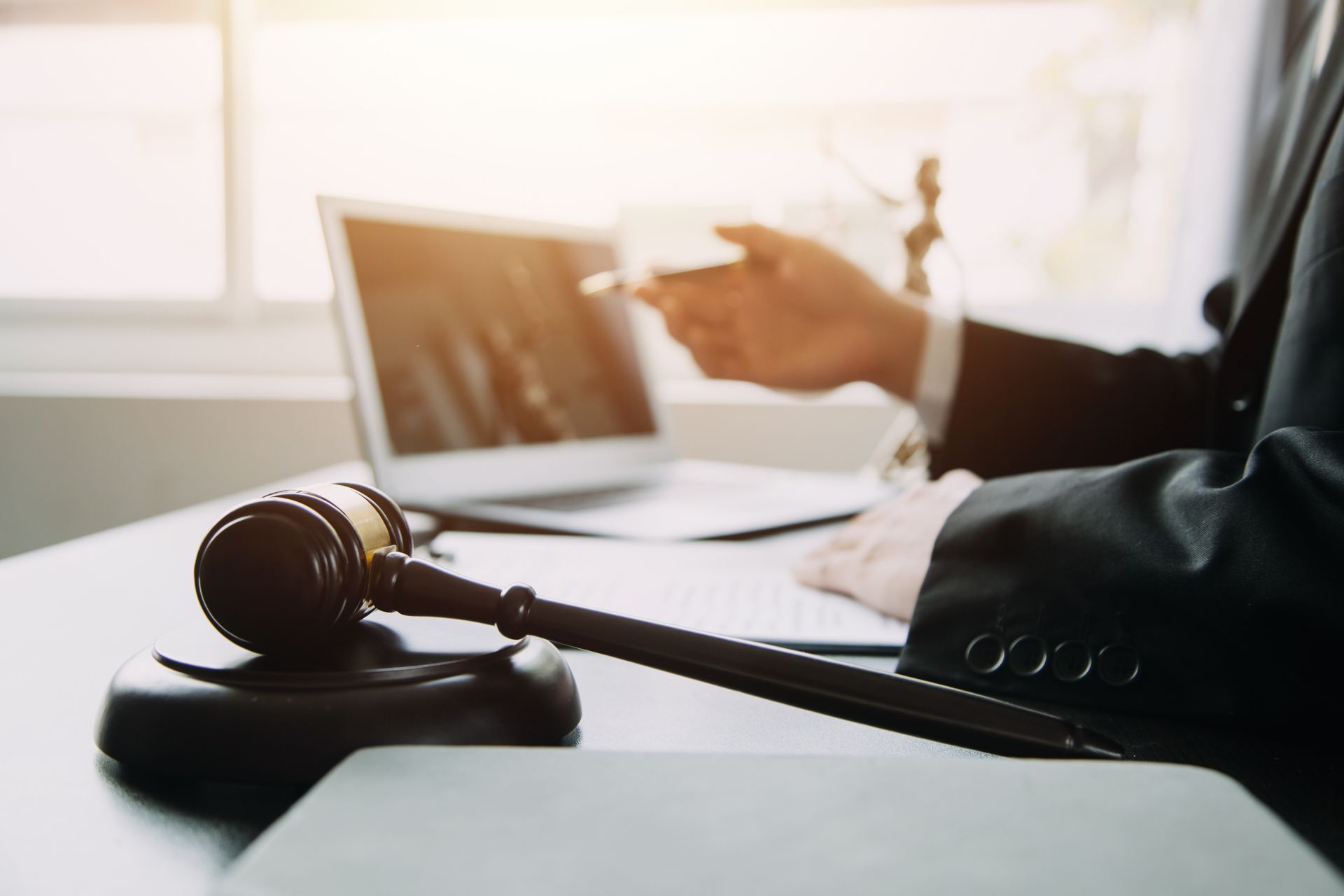Gavel on desk beside a laptop, with a person in a suit pointing at the screen Gavel on desk beside a laptop, with a person in a suit pointing at the screen