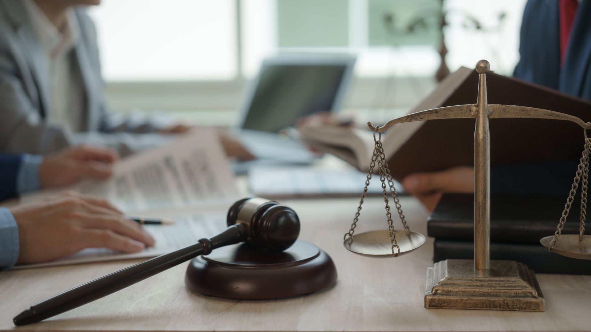 Lawyer’s desk with gavel, scales of justice, and people reviewing documents in the background Lawyer’s desk with gavel, scales of justice, and people reviewing documents in the background