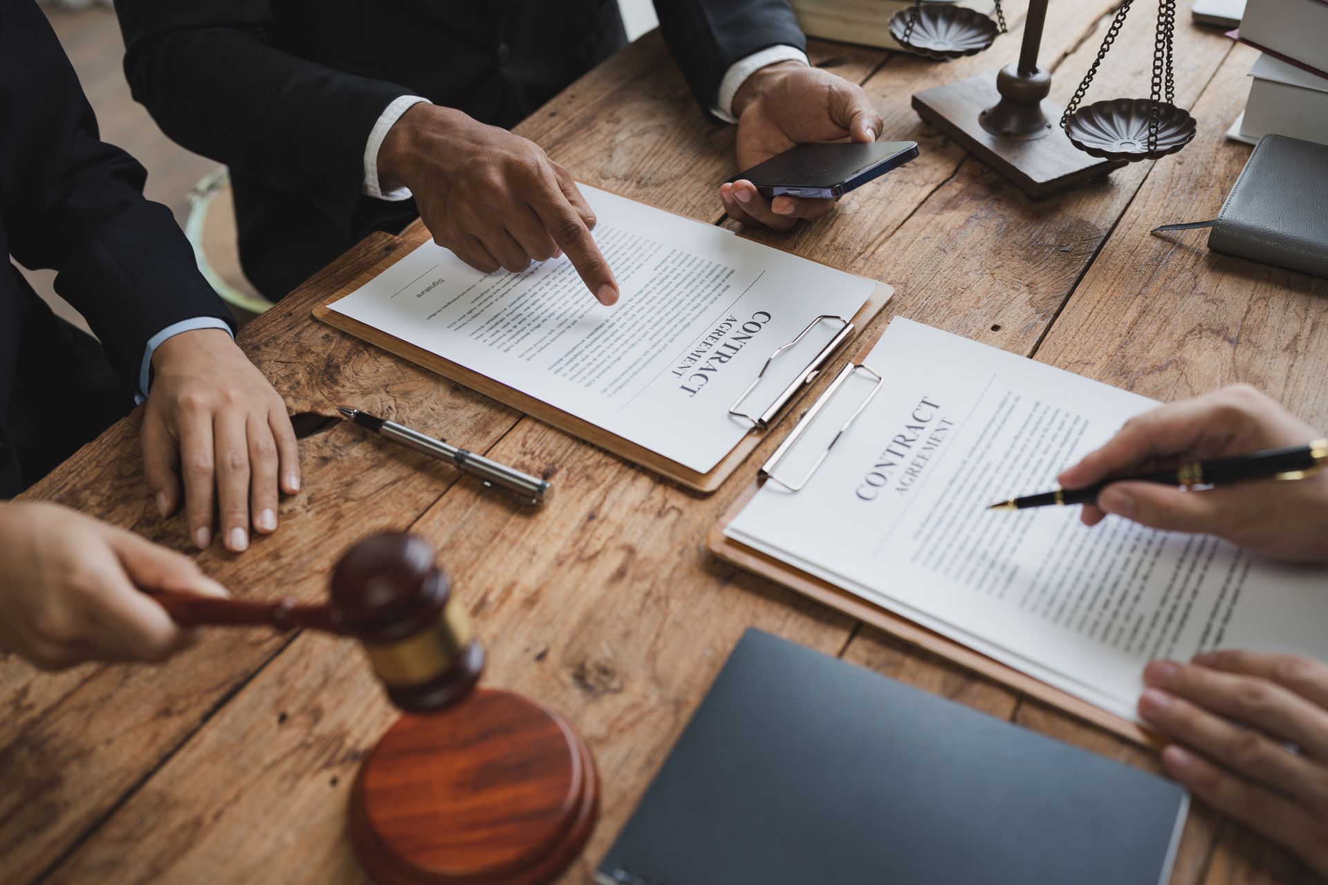 Lawyers reviewing documents around a wooden table with a gavel and pen in a meeting room Lawyers reviewing documents around a wooden table with a gavel and pen in a meeting room