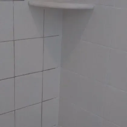 A bathroom with white tiles and a shelf on the wall.