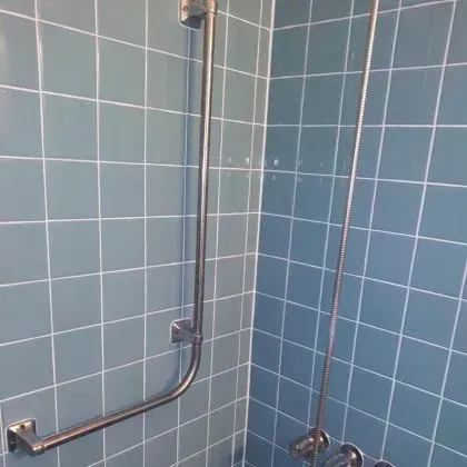 A shower with blue tiles and a stainless steel hand rail