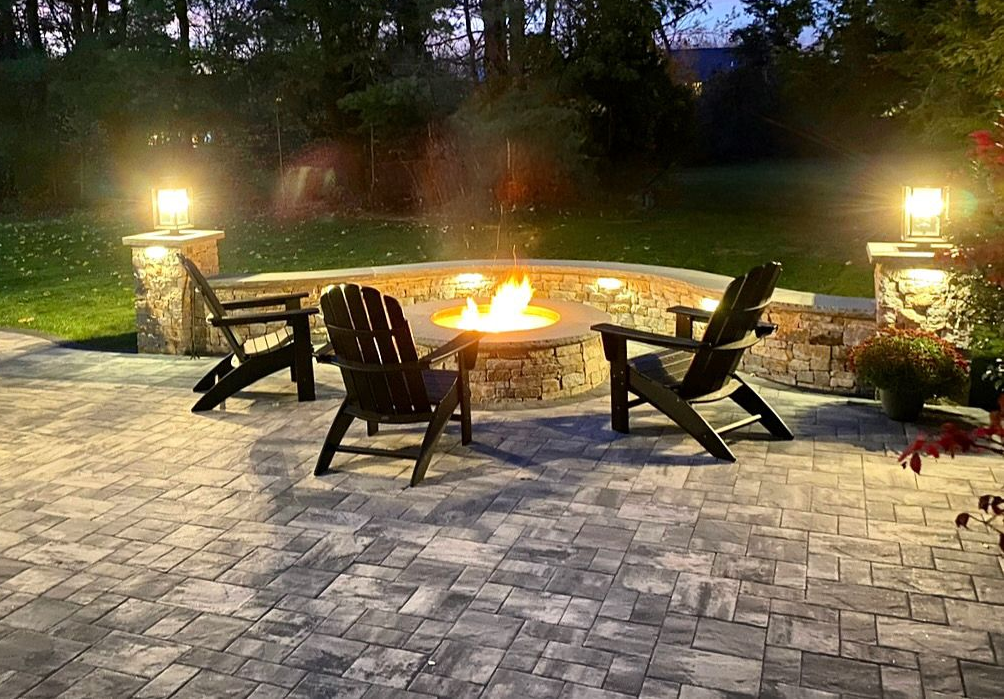 Backyard fire pit with Adirondack chairs on a stone patio at dusk, lit by lanterns