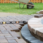 Paver patio edge with a level, curved stone border and a wheelbarrow in the background