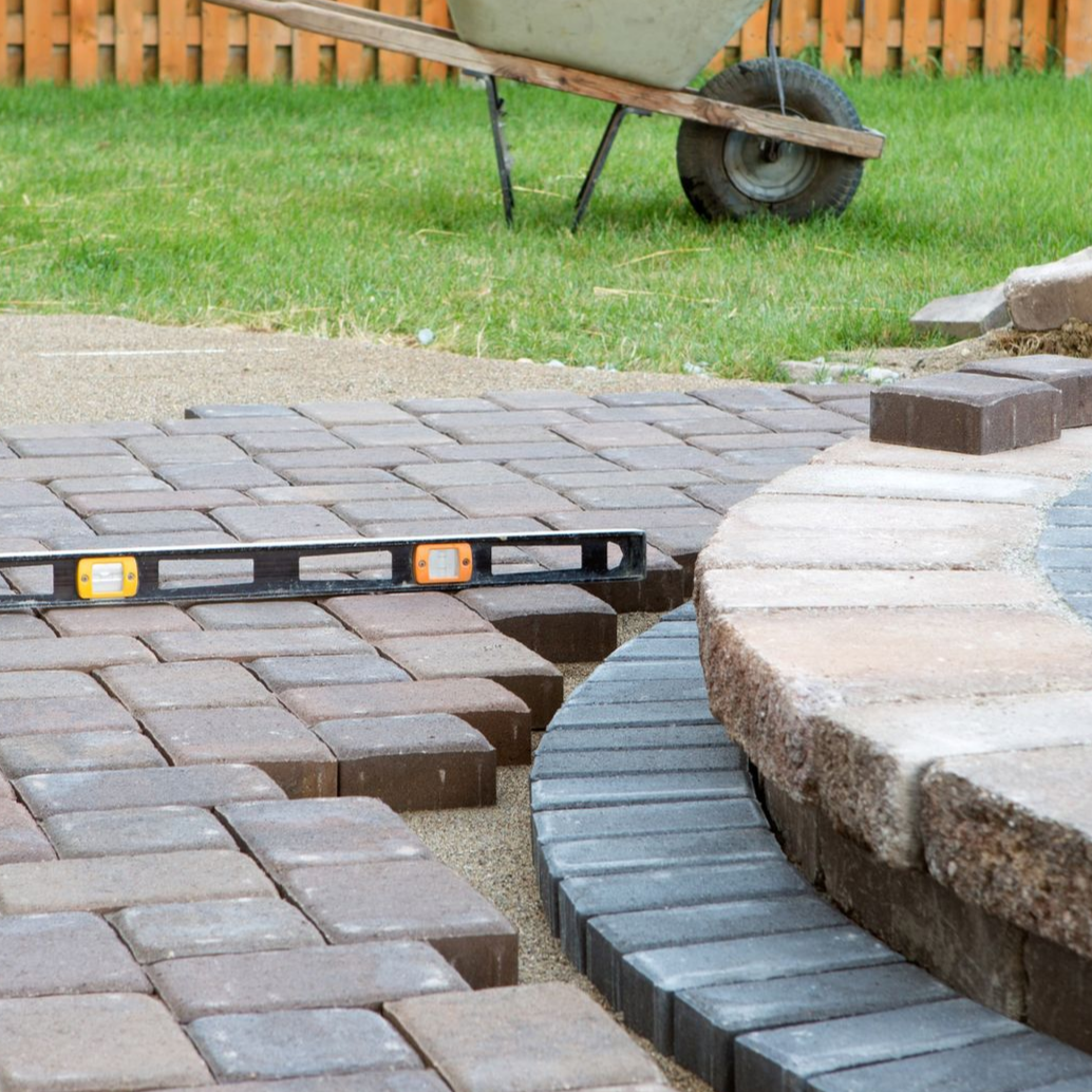 Paver patio edge with a level, curved stone border and a wheelbarrow in the background