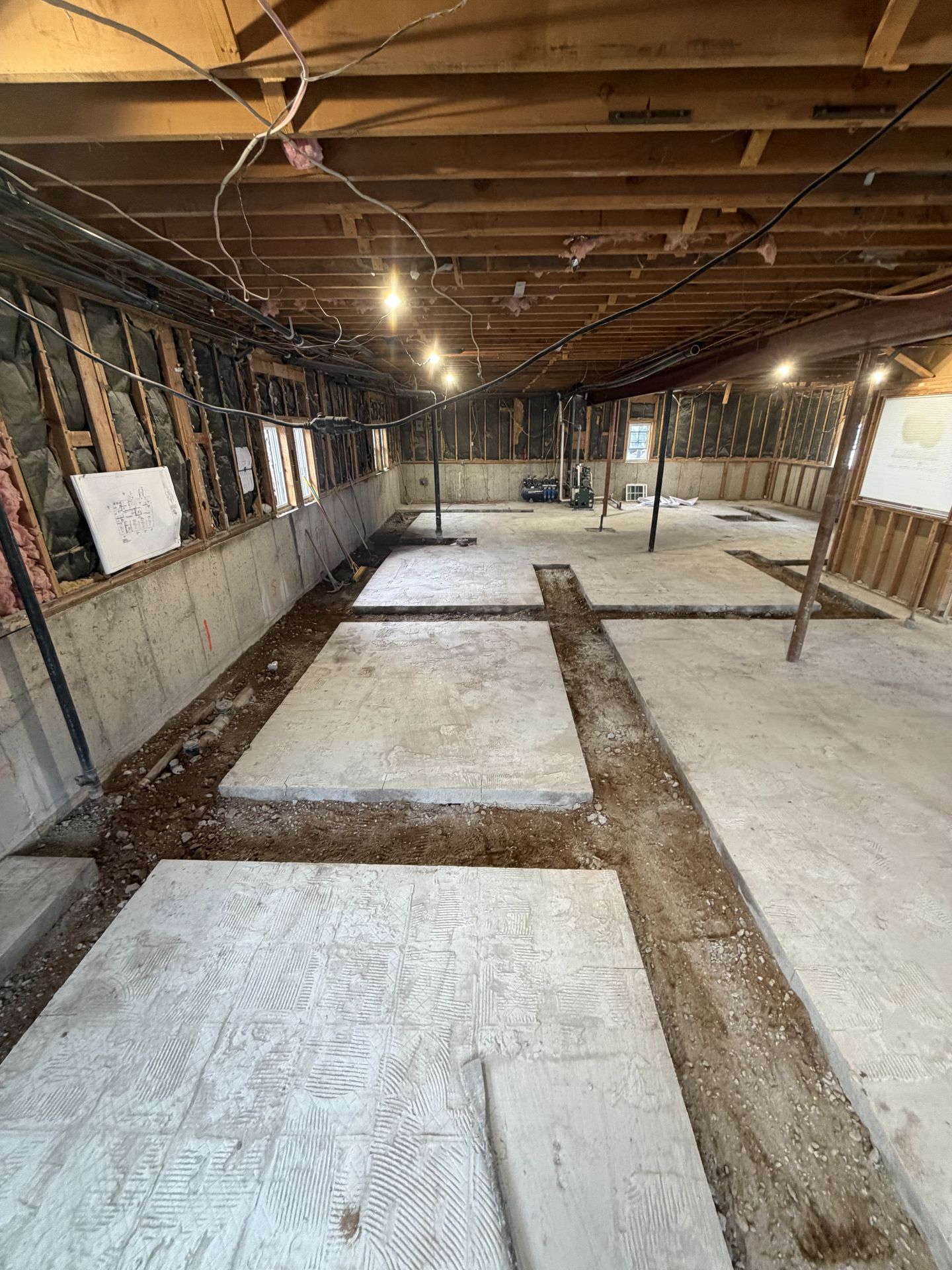 Basement with exposed ceiling joists, concrete floor trenches, and white utility panels under renovation