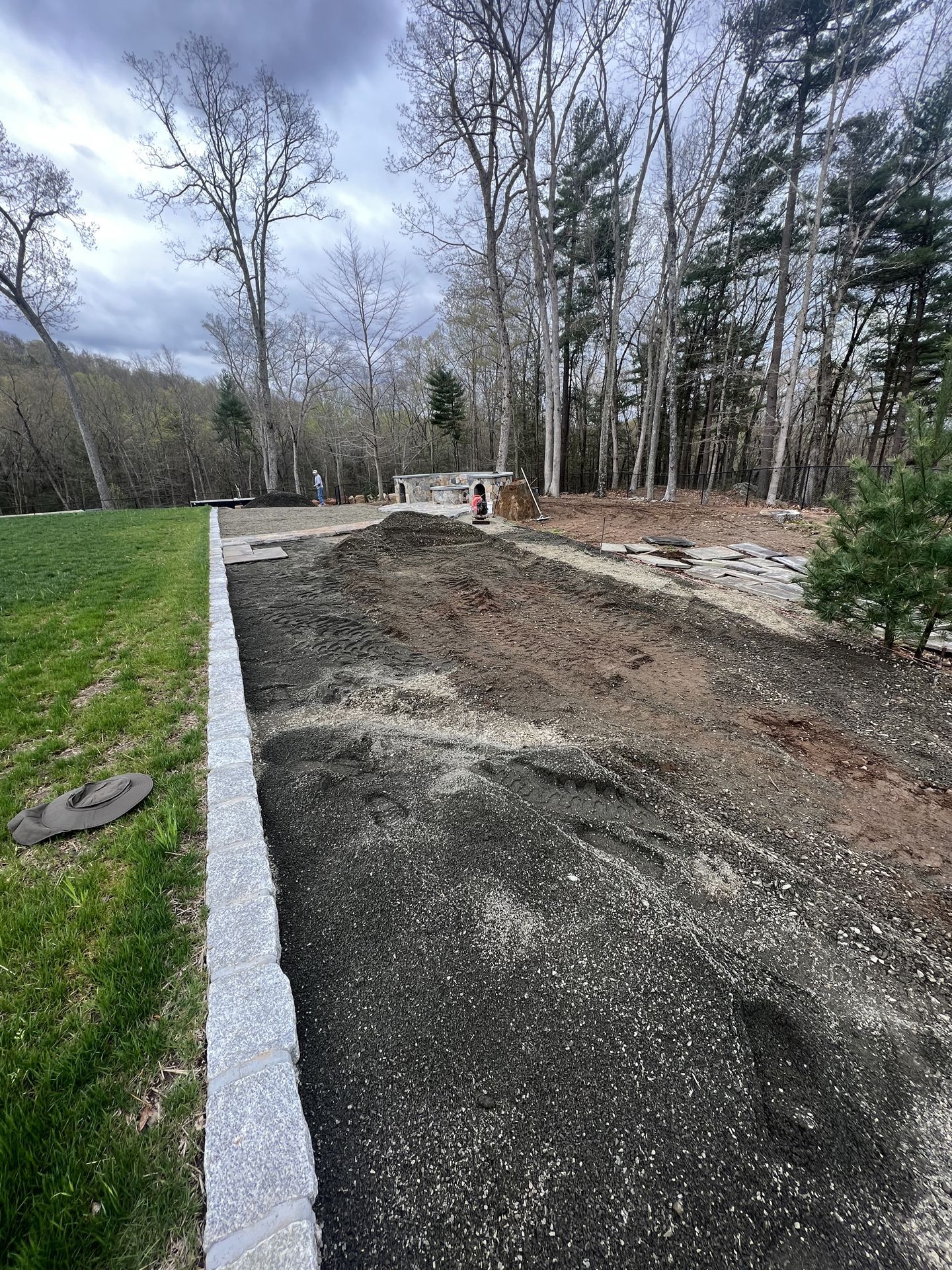 Gravel driveway beside a grassy strip, with trees and bare ground under a cloudy sky