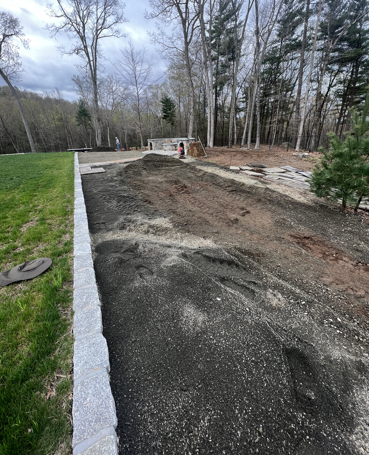 Gravel driveway under construction beside a green lawn and leafless trees