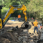 Yellow JCB excavator clearing rocks at a construction site with workers in orange safety vests