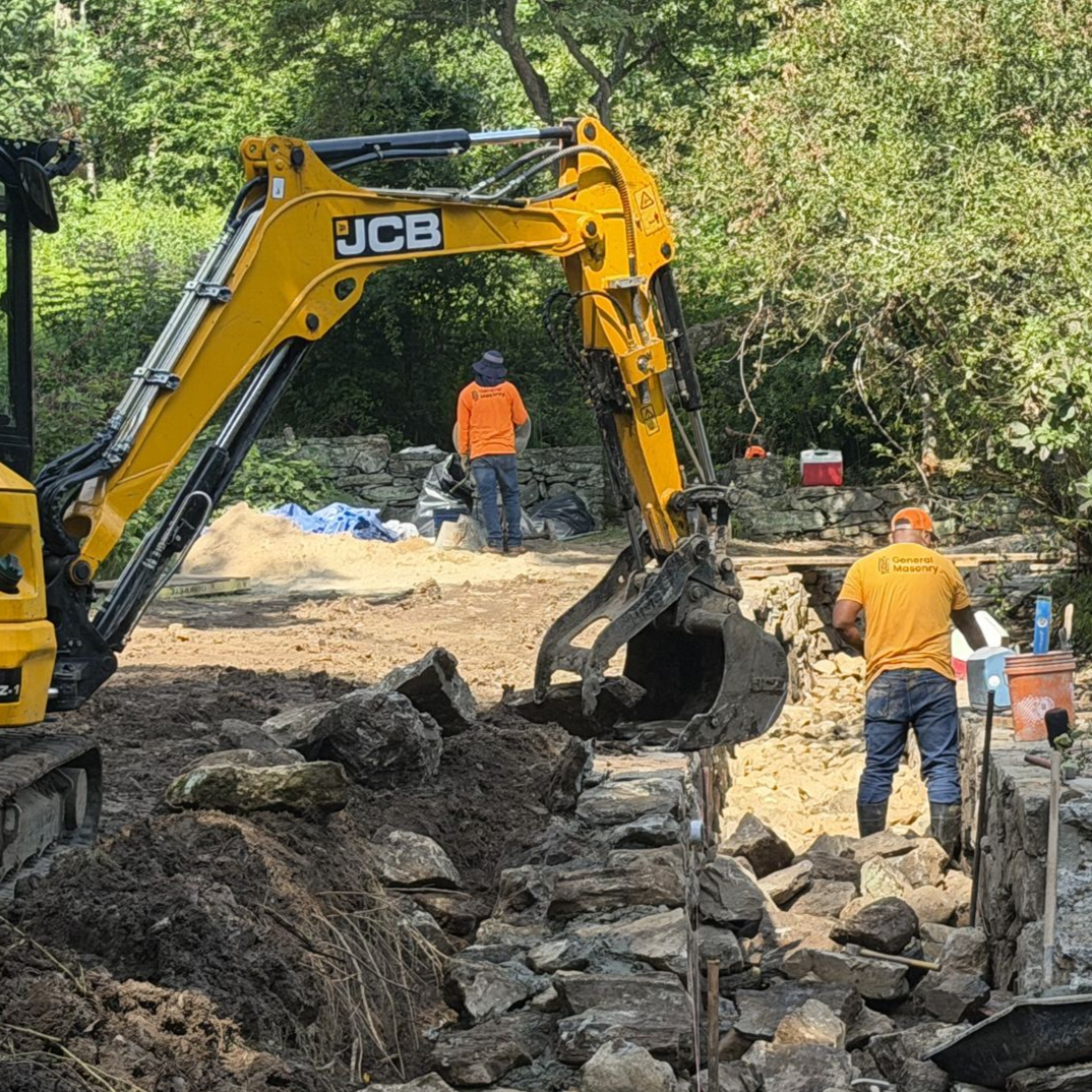 Yellow JCB excavator clearing rocks at a construction site with workers in orange safety vests