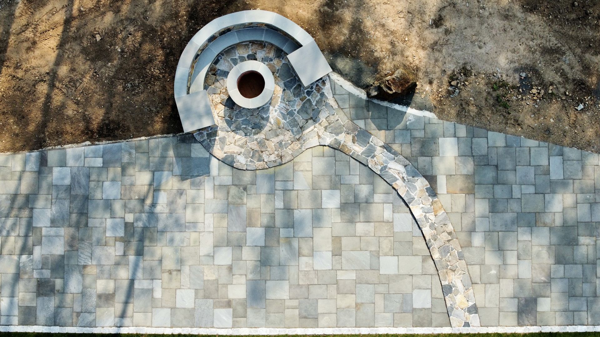Abstract mosaic stone sculpture with a circular eye-like opening on a rough stone wall