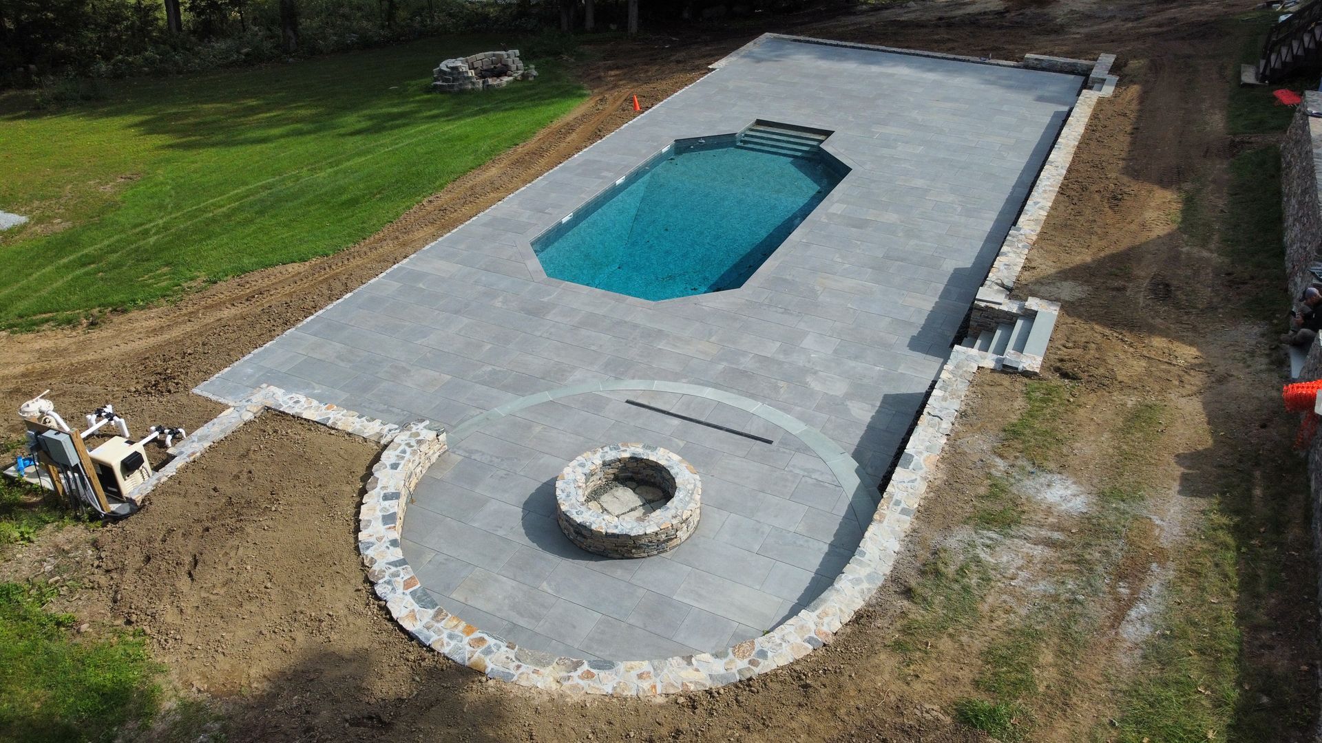 Backyard in-ground pool under construction with concrete deck and circular fire pit area