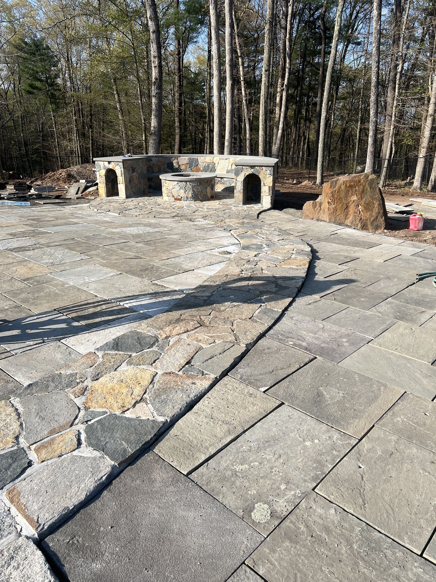 Stone patio and built-in outdoor grill area in a wooded yard, with large pavers in the foreground