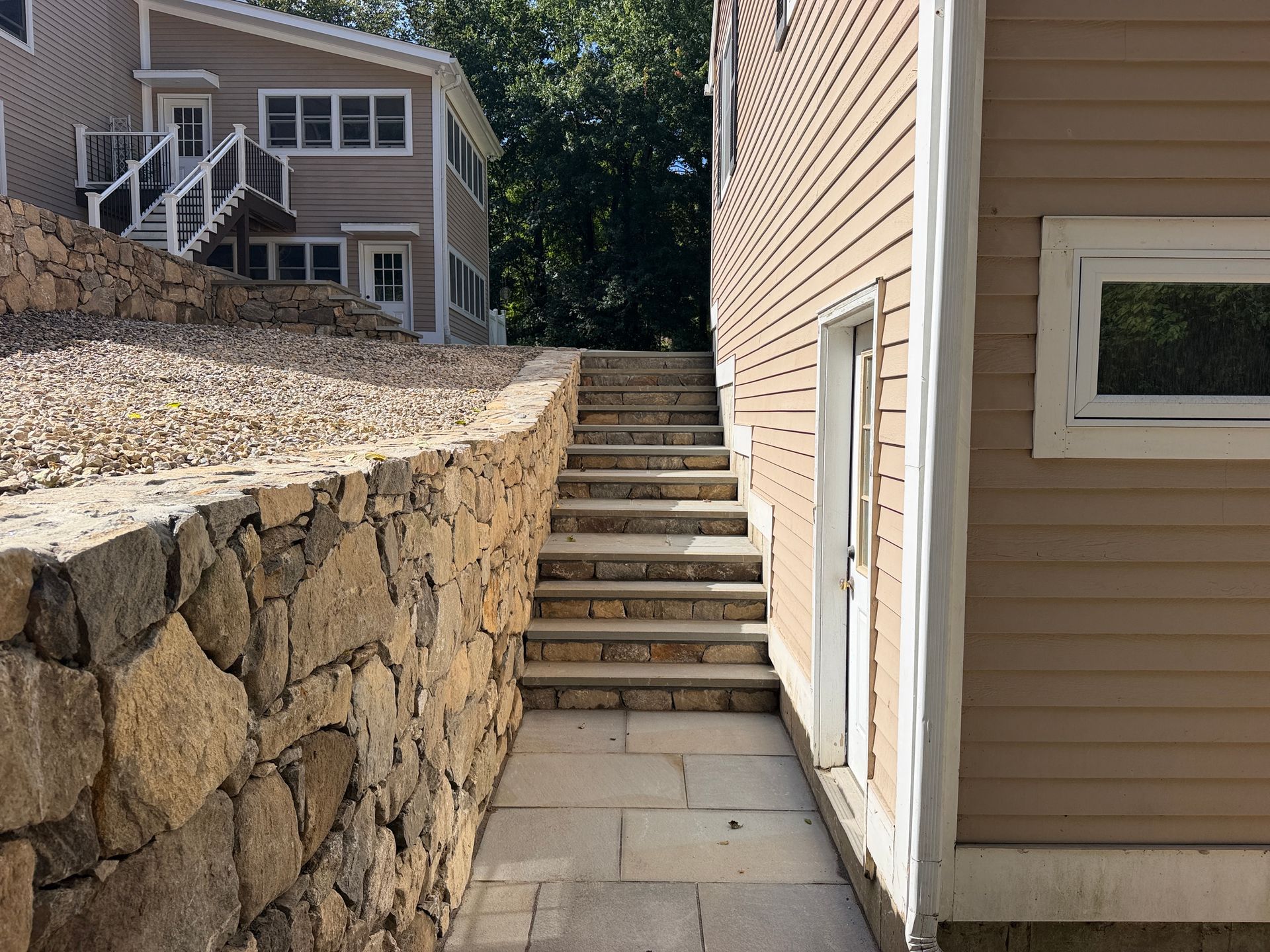 Stone retaining wall and outdoor staircase between tan houses in a residential yard