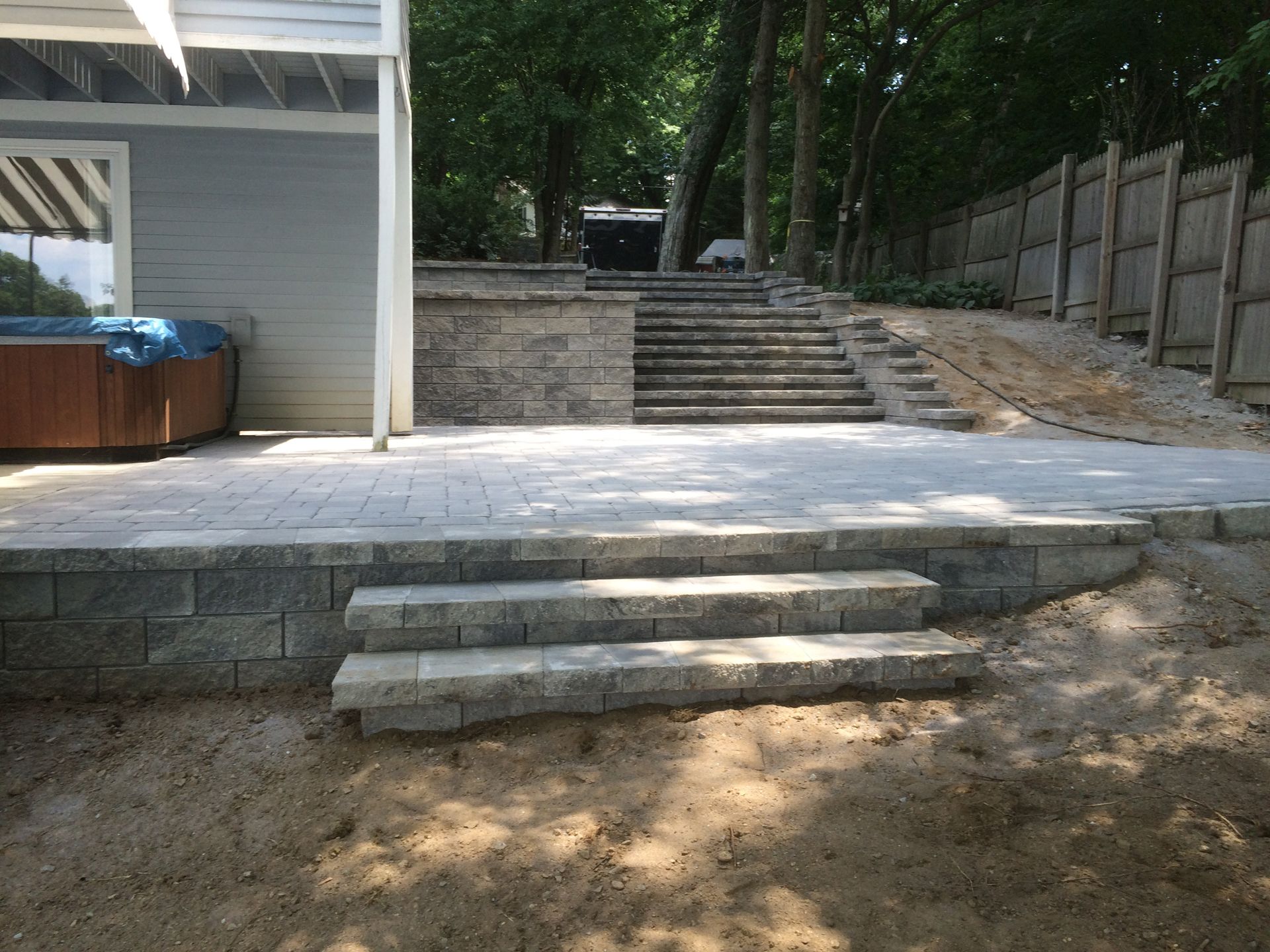 Outdoor stone steps leading to a raised patio beside a house and retaining wall