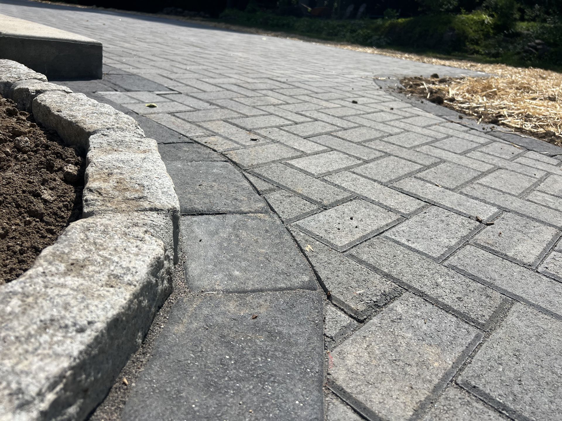 Curved stone and brick walkway edging a landscaped path with dark soil on the left and gravel on the right