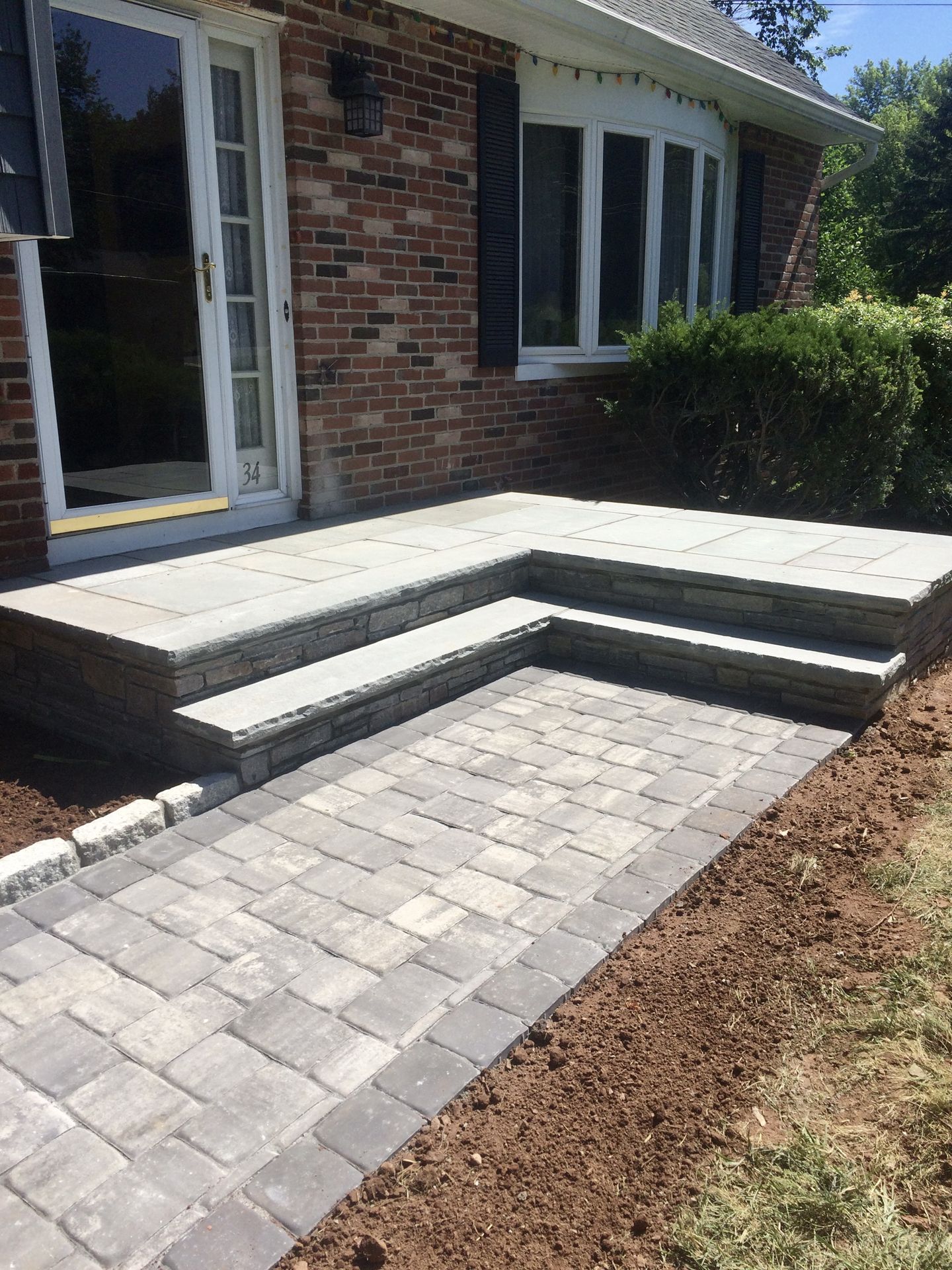 Brick house entrance with newly paved stone walkway and three concrete steps leading to a patio.