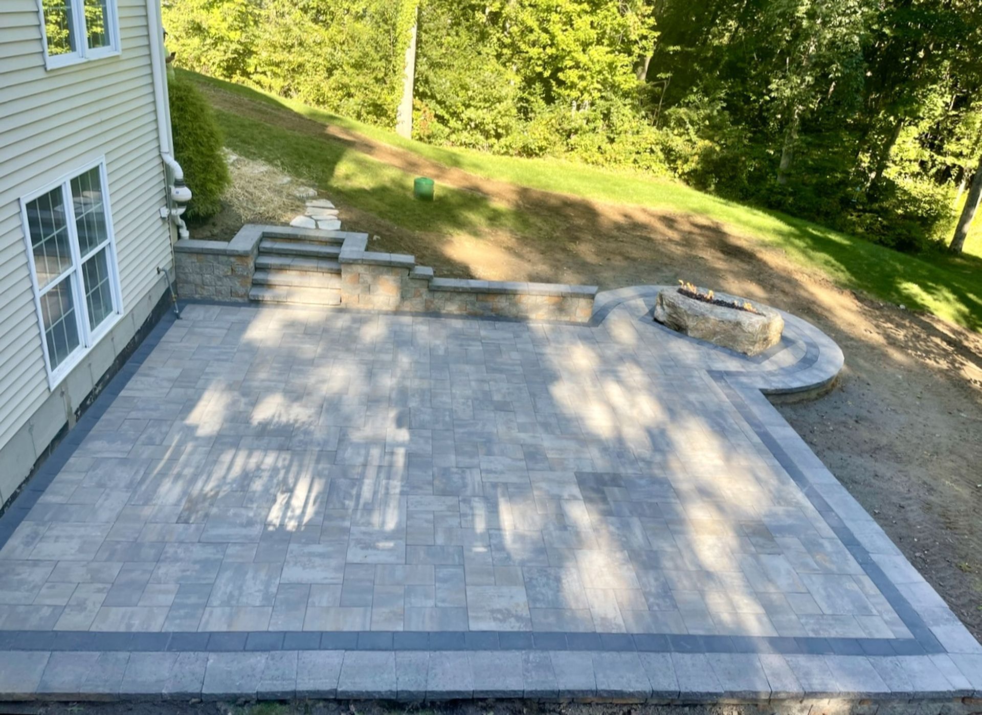 Large gray stone patio beside a house, with steps and a curved seating area overlooking a grassy yard.