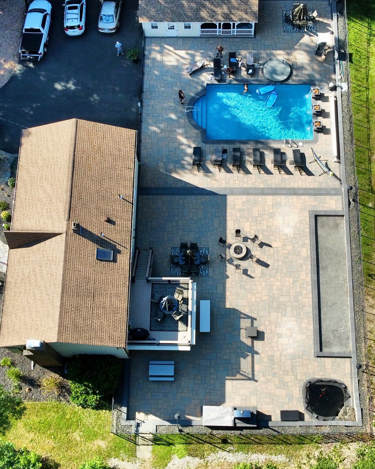 Aerial view of a backyard patio with a pool, lounge chairs, and a house beside it.