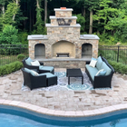 Outdoor stone fireplace with black wicker seating around a pool patio and green trees behind
