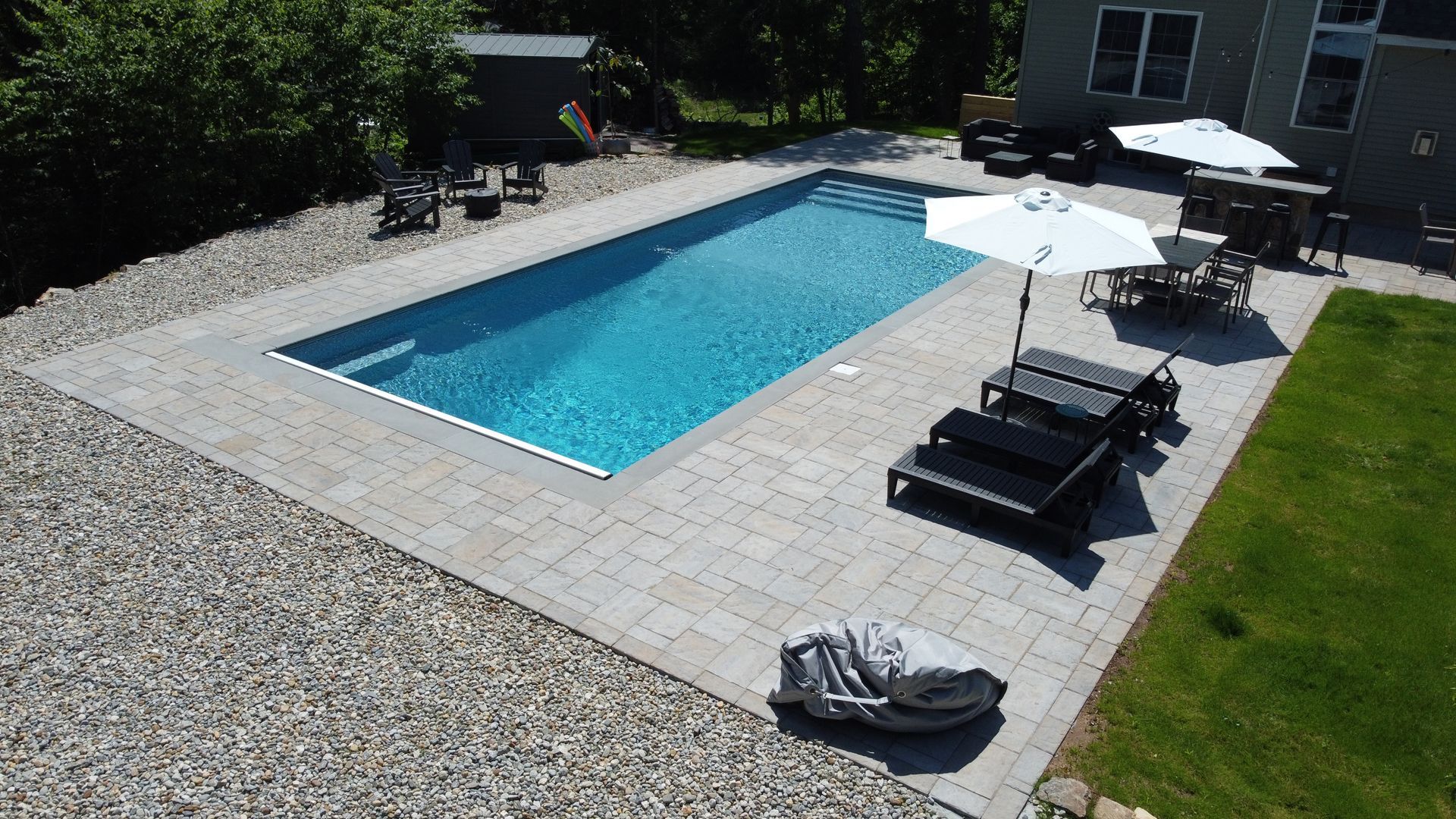 Backyard swimming pool with loungers, umbrella, and gravel patio in sunlight
