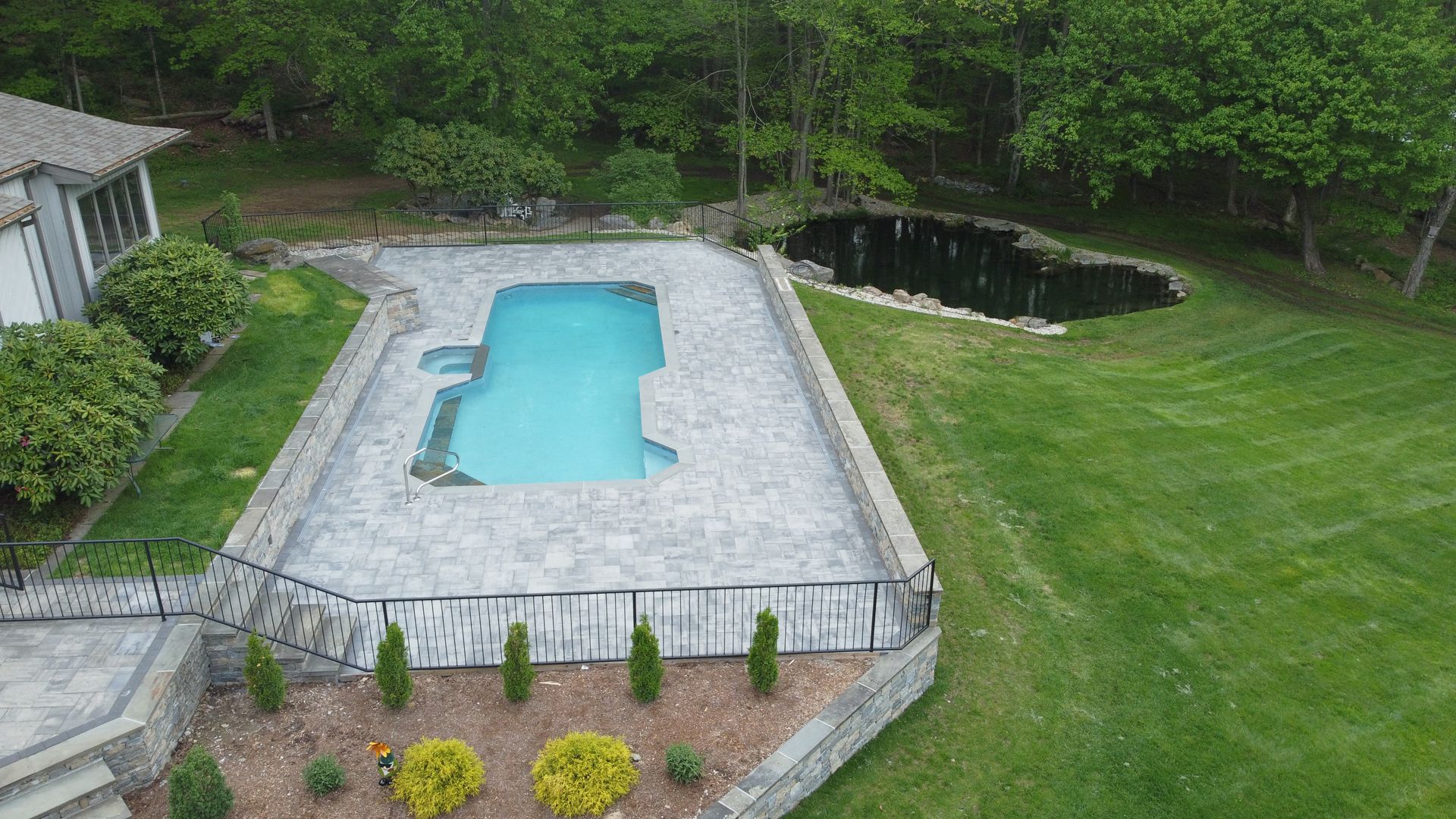 Backyard swimming pool with light blue water, stone deck, and green lawn surrounded by trees