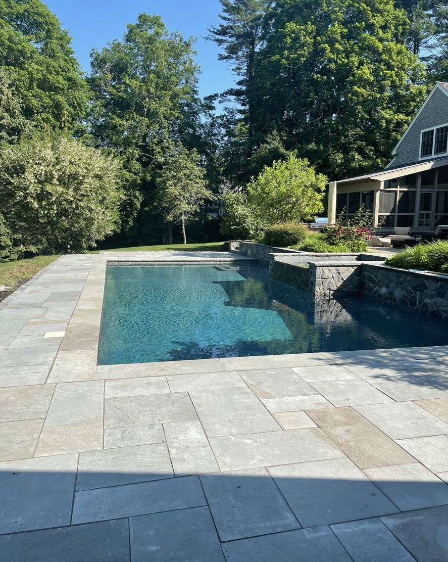 Backyard pool with blue water, stone patio, and a house surrounded by trees