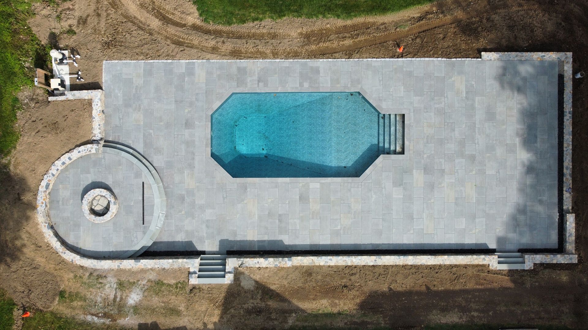 Aerial view of a rectangular backyard pool beside a circular hot tub on a large concrete patio.